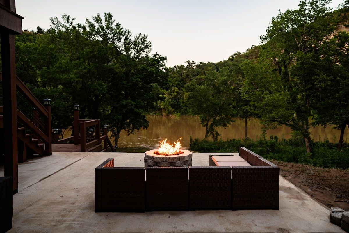 An outdoor seating area with a fire pit and a view of a lake surrounded by trees.