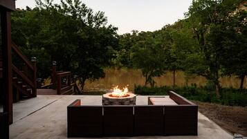 An outdoor seating area with a fire pit and a view of a lake surrounded by trees.