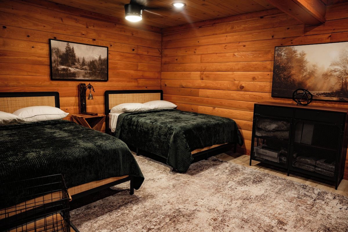 A wooden cabin room with two beds, a nightstand, and a bookshelf.