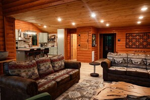 Ein Innenraum einer Holzblockhütte mit Wohnzimmer, Küche und Essbereich.