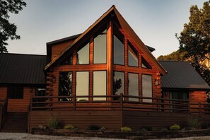 A log cabin with a prominent gable roof, large windows, and a wooden deck.