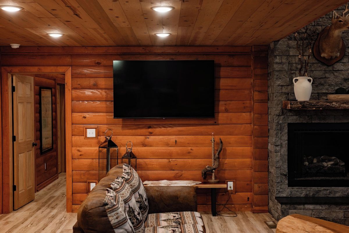 Ein gemütliches Blockhaus-Interieur mit einer Holzwand, einem montierten Fernseher, einem Kamin und einer Couch.
