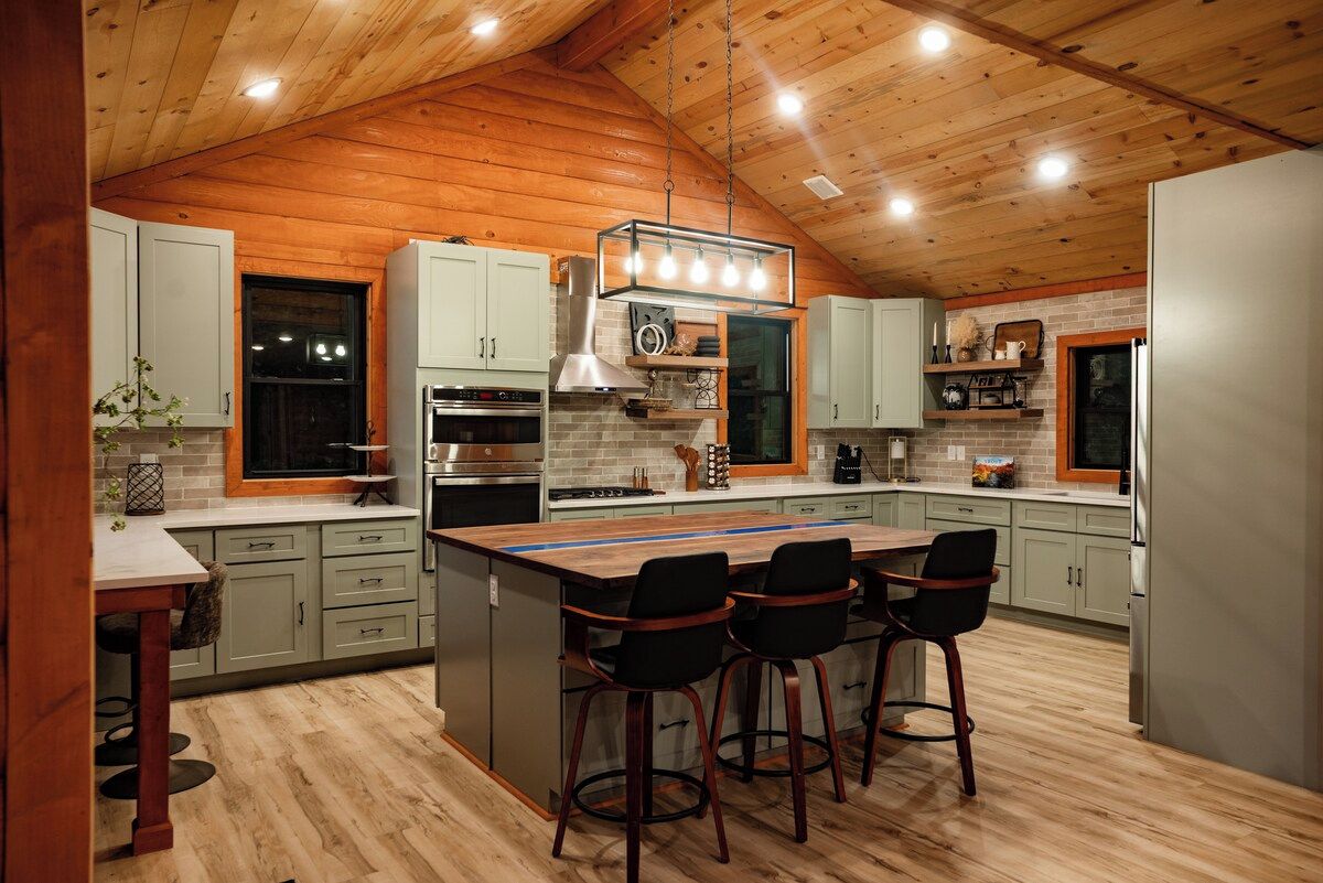 A modern kitchen with wooden ceiling beams, a central island with bar stools, and built-in appliances.