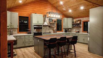 A modern kitchen with wooden ceiling beams, a central island with bar stools, and built-in appliances.