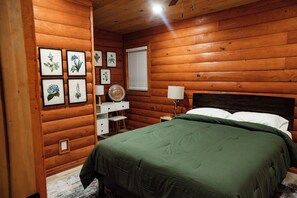 A wooden cabin bedroom with a bed, a dresser, a lamp, and framed botanical prints on the wall.
