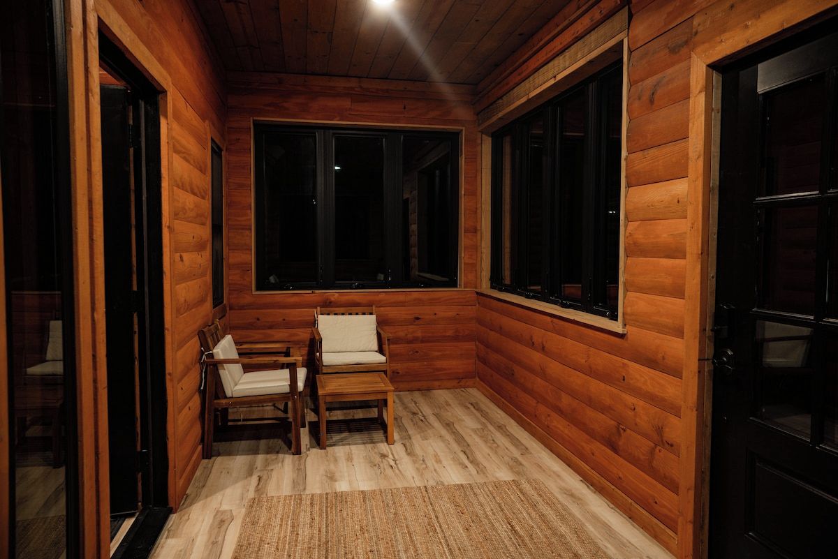 A wooden cabin interior with a bench, a table, and a large window.