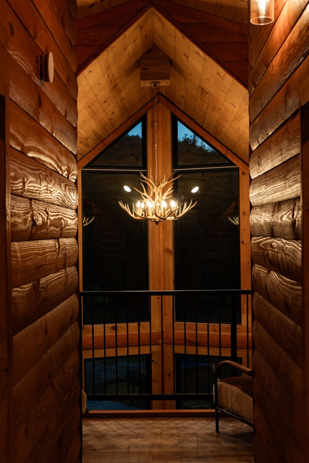 Een houten interieur met een kroonluchter, een balkon met een hekwerk en een raam met uitzicht.