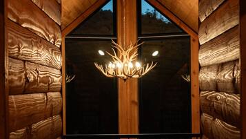 Een houten interieur met een kroonluchter, een balkon met een hekwerk en een raam met uitzicht.