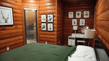 Habitación de cabaña de madera con una cama, una mesita de noche, una lámpara e impresiones botánicas enmarcadas en la pared.