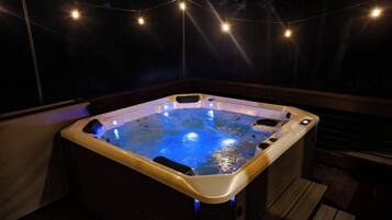 Un jacuzzi con terraza de madera y luces cálidas.