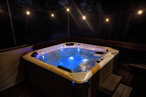 A hot tub with a wooden deck and string lights.
