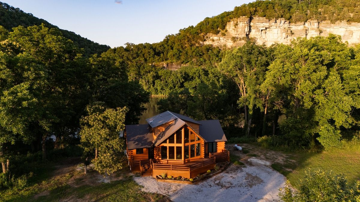 A cabin with a large deck and a view of a forested hill.