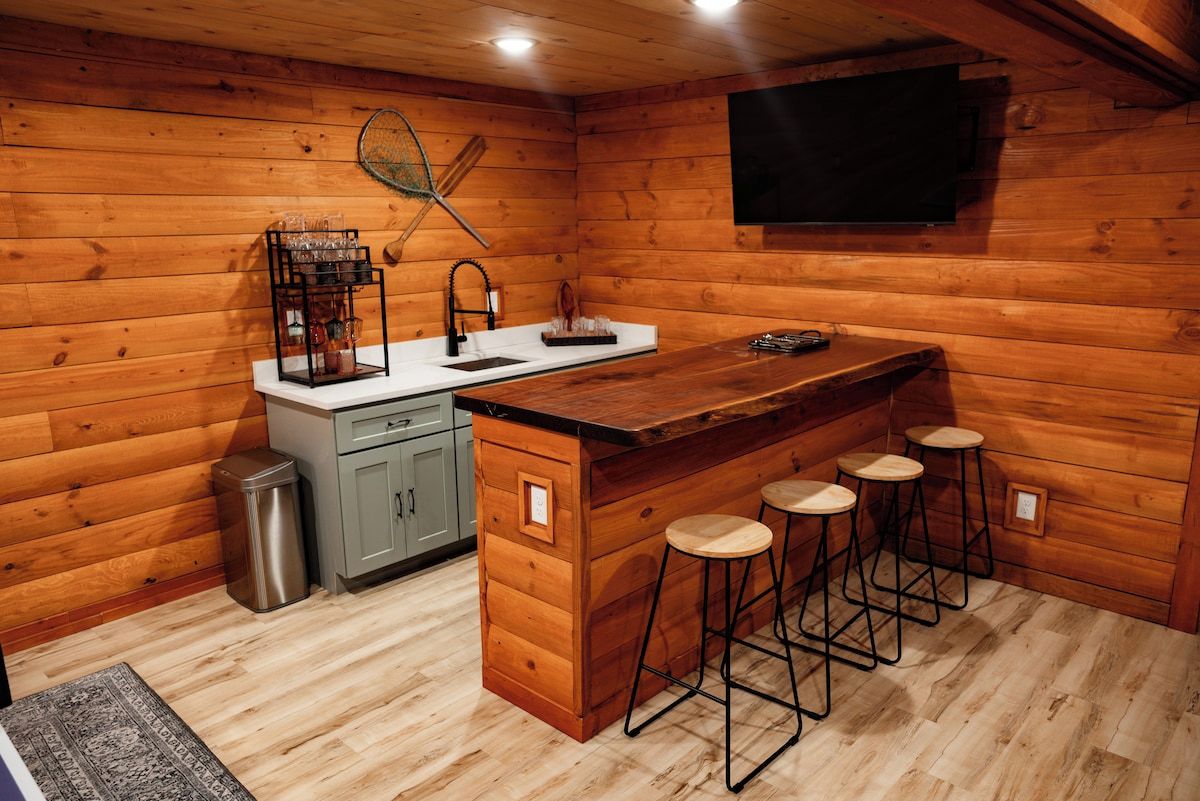 A wooden cabin interior with a kitchen area, bar stools, and a television mounted on the wall.
