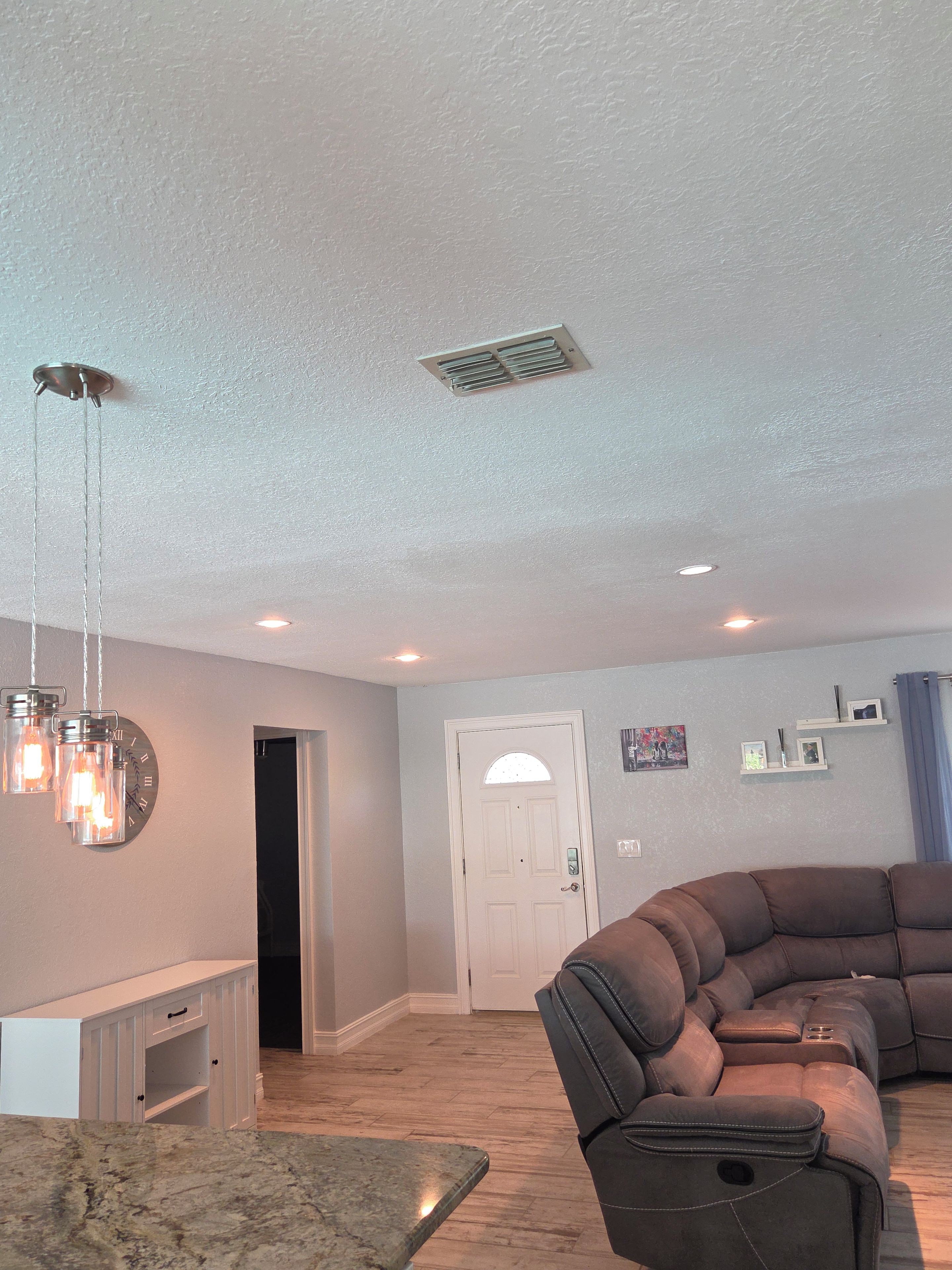 A living room with a sectional sofa, a marble coffee table, pendant lights, a white door, and a wall-mounted clock.