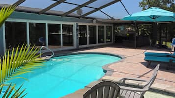 A swimming pool with a glass enclosure, lounge chairs, and a patio area.