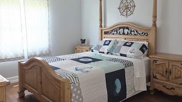 A bedroom with a wooden four-poster bed, a ceiling fan, a compass wall decoration, and a nightstand with a lamp.