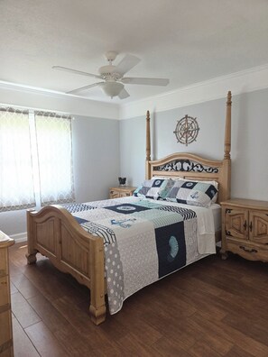 A bedroom with a wooden four-poster bed, a ceiling fan, a compass wall decoration, and a nightstand with a lamp.