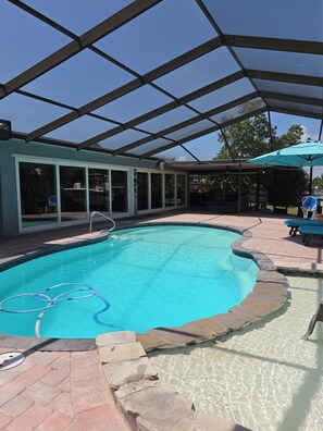 A swimming pool with a glass enclosure, a diving board, and a patio area with seating.