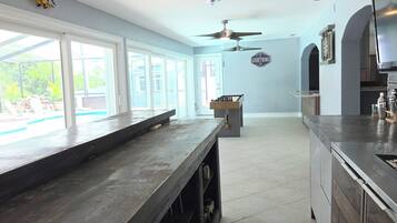 A spacious kitchen with a bar area, ceiling fans, and a view through large windows.