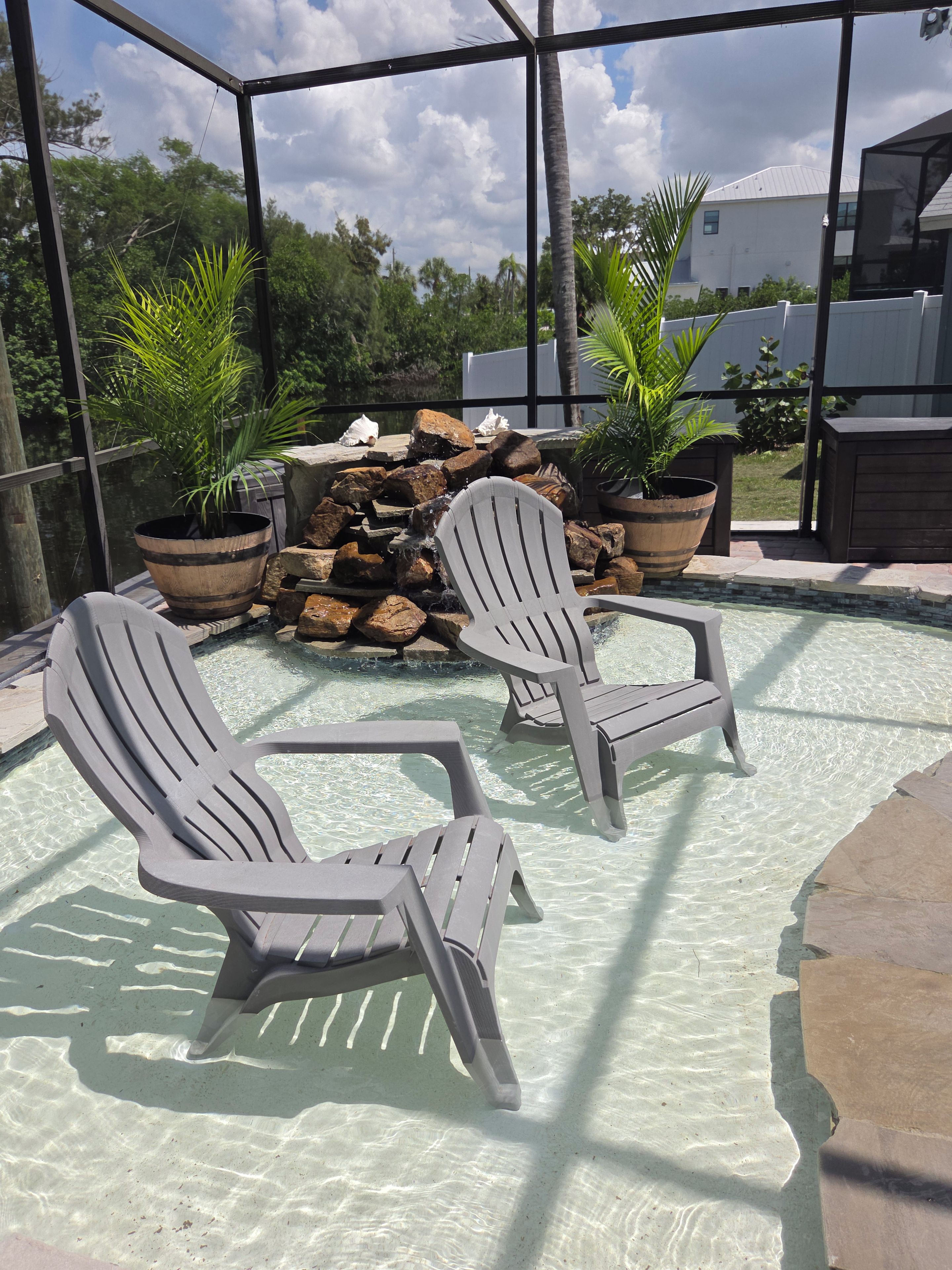 A pool area with two Adirondack chairs, a small waterfall feature, and potted plants.