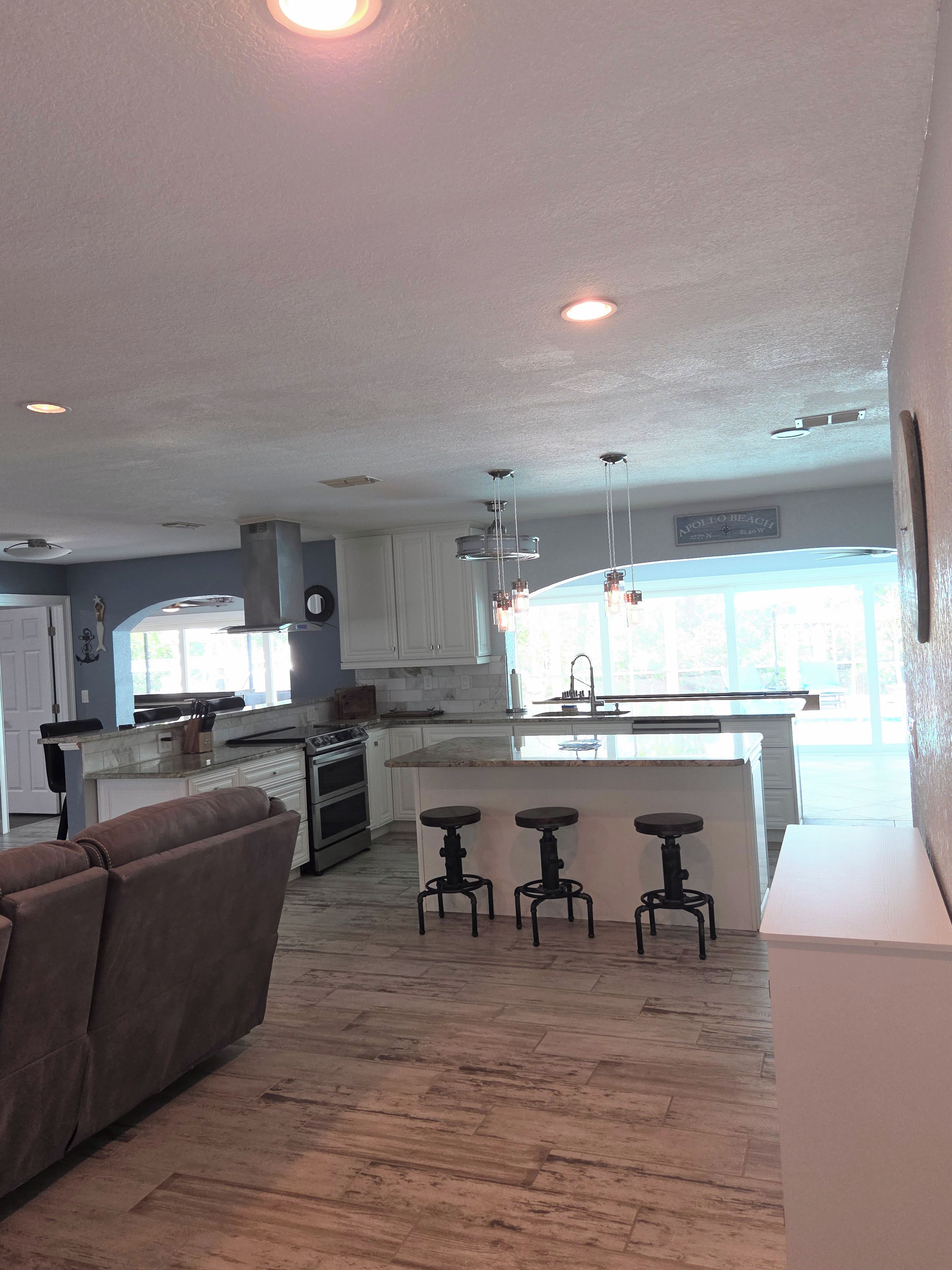 A modern kitchen with white cabinets, a central island with stools, and a dining area with a brown leather couch.