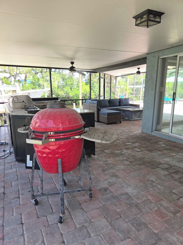 A covered patio area with a barbecue grill, outdoor furniture, and a view of the outdoors.