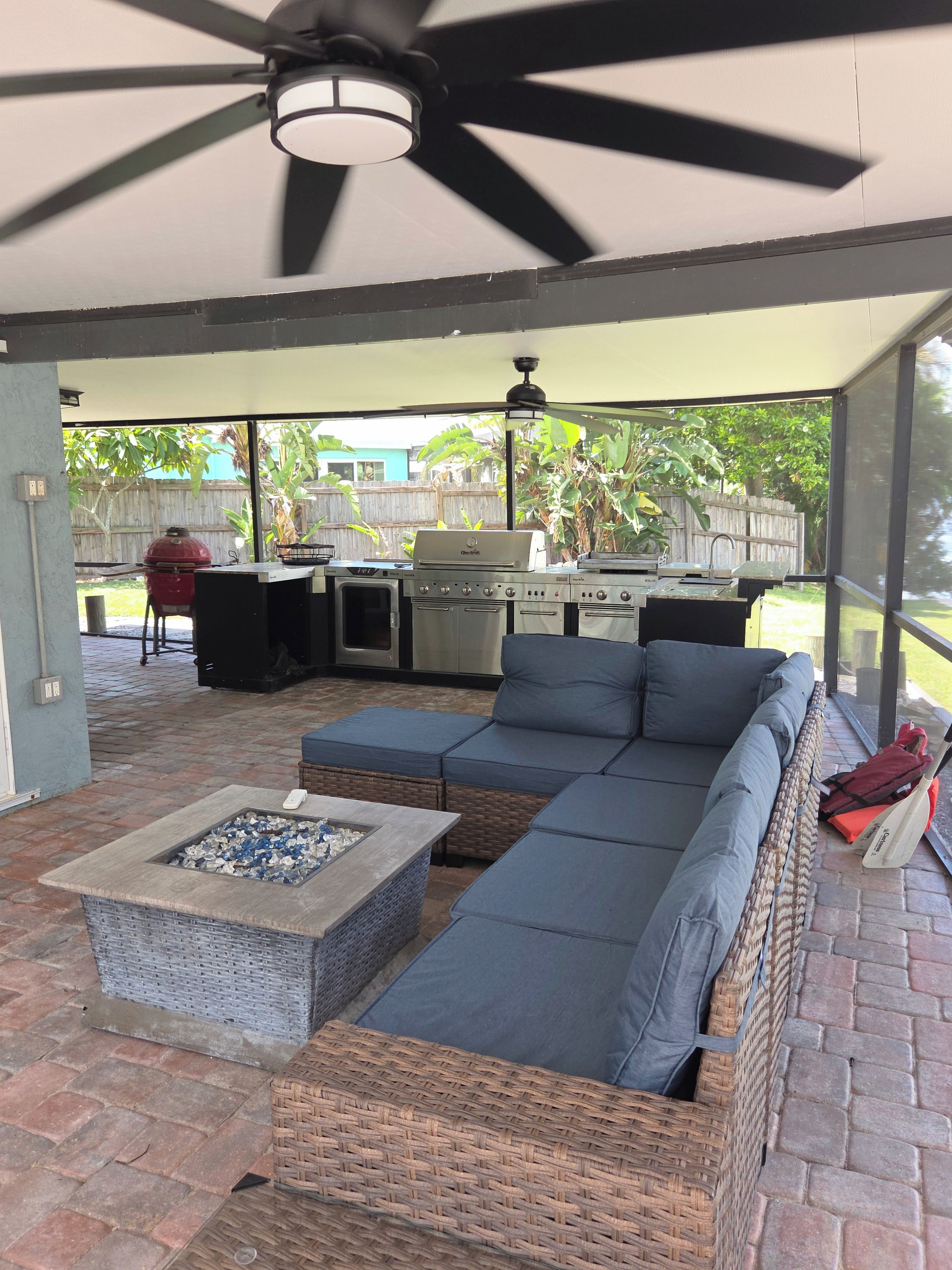 A covered outdoor patio with a sectional sofa, a fire pit, and a grill.