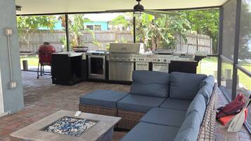 A covered outdoor patio with a sectional sofa, a fire pit, and a grill.