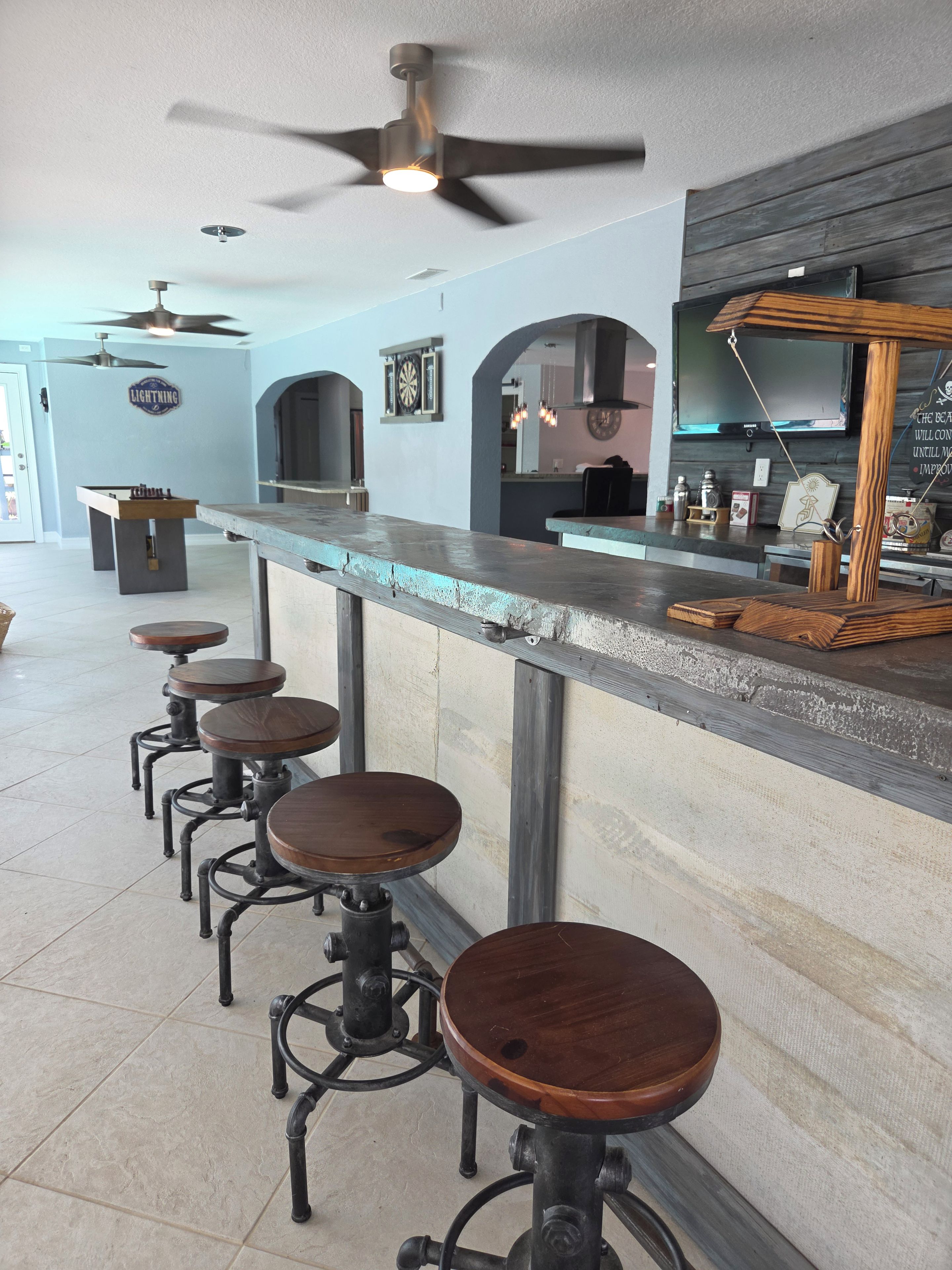 A bar area with stools, a ceiling fan, and a dartboard on the wall.
