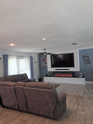 A living room with a large flat-screen TV, a fireplace, and a sofa.