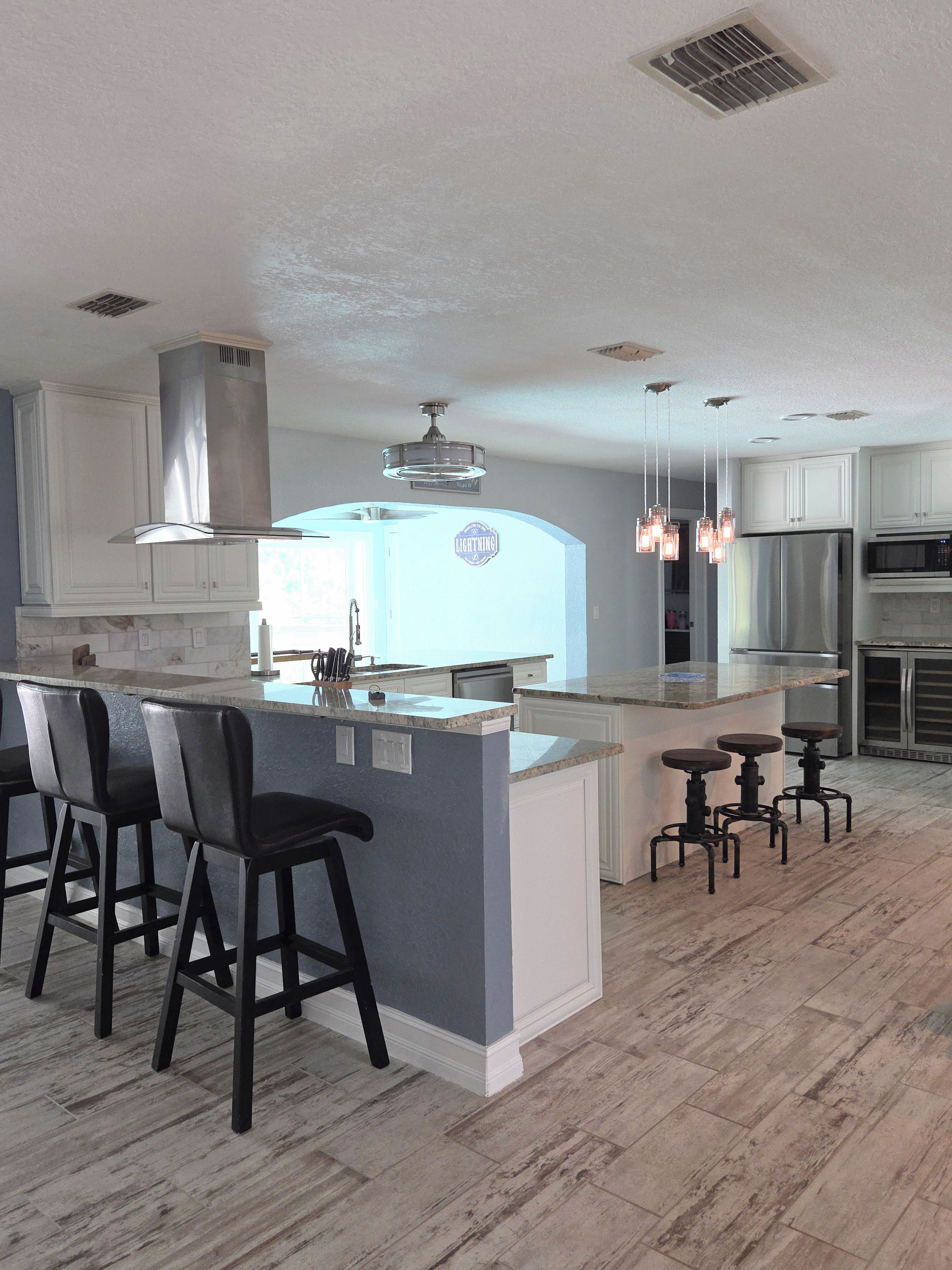 A modern kitchen with a central island, bar stools, and pendant lighting.