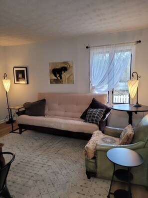 A living room with a sofa, a small round table, a green armchair, a patterned rug, a framed picture, and a painting of a dog. - Peaceful 1-bedroom back house with AC in charming Versailles (Versailles)