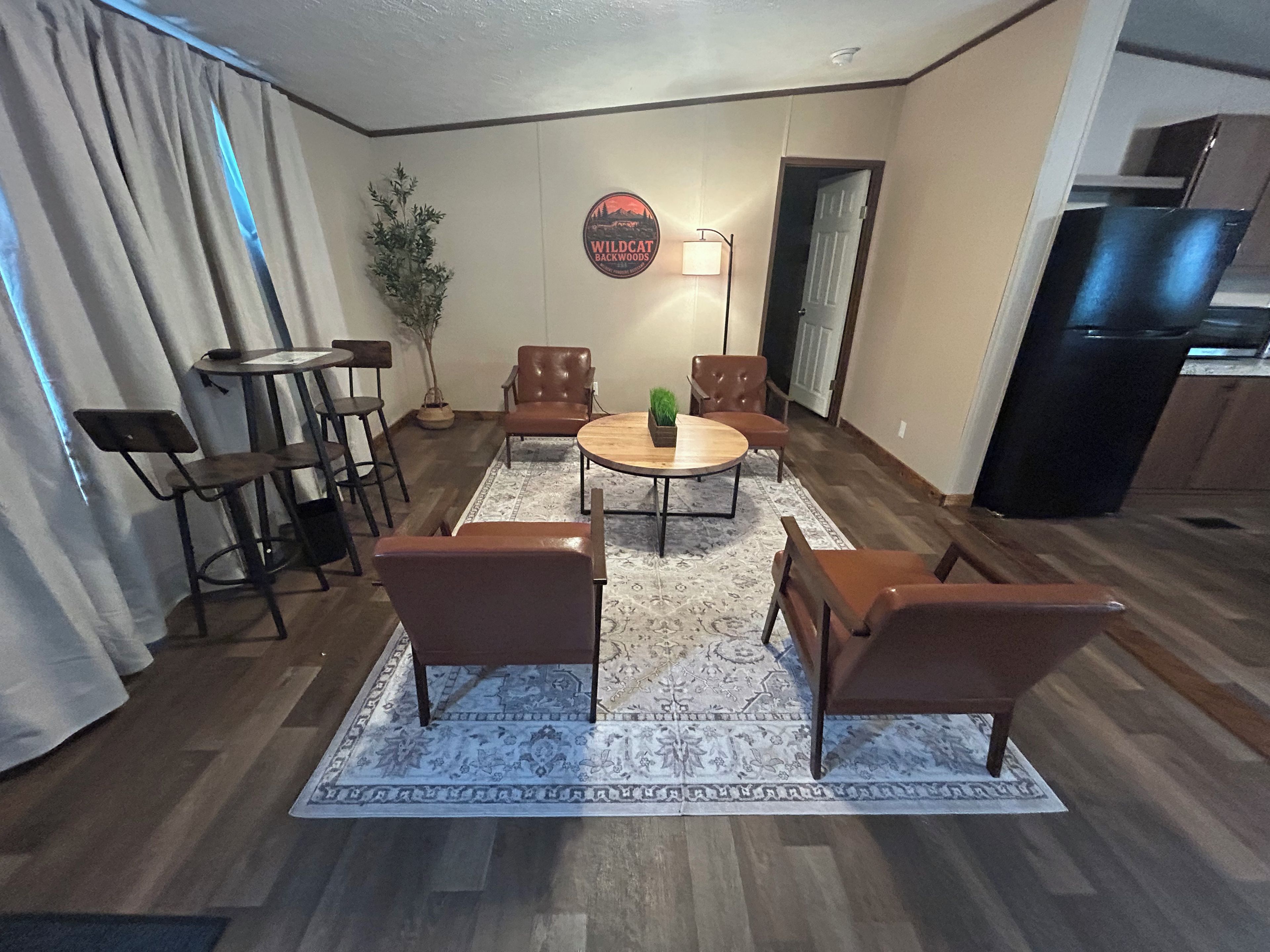 Ein Wohnzimmer mit rundem Couchtisch, vier braunen Sesseln, einer Topfpflanze und einem an der Wand befestigten Schild.