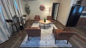 Ein Wohnzimmer mit rundem Couchtisch, vier braunen Sesseln, einer Topfpflanze und einem an der Wand befestigten Schild.