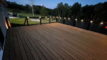 Eine Holzterrasse mit Lichterketten, umgeben von einem Zaun und Bäumen.