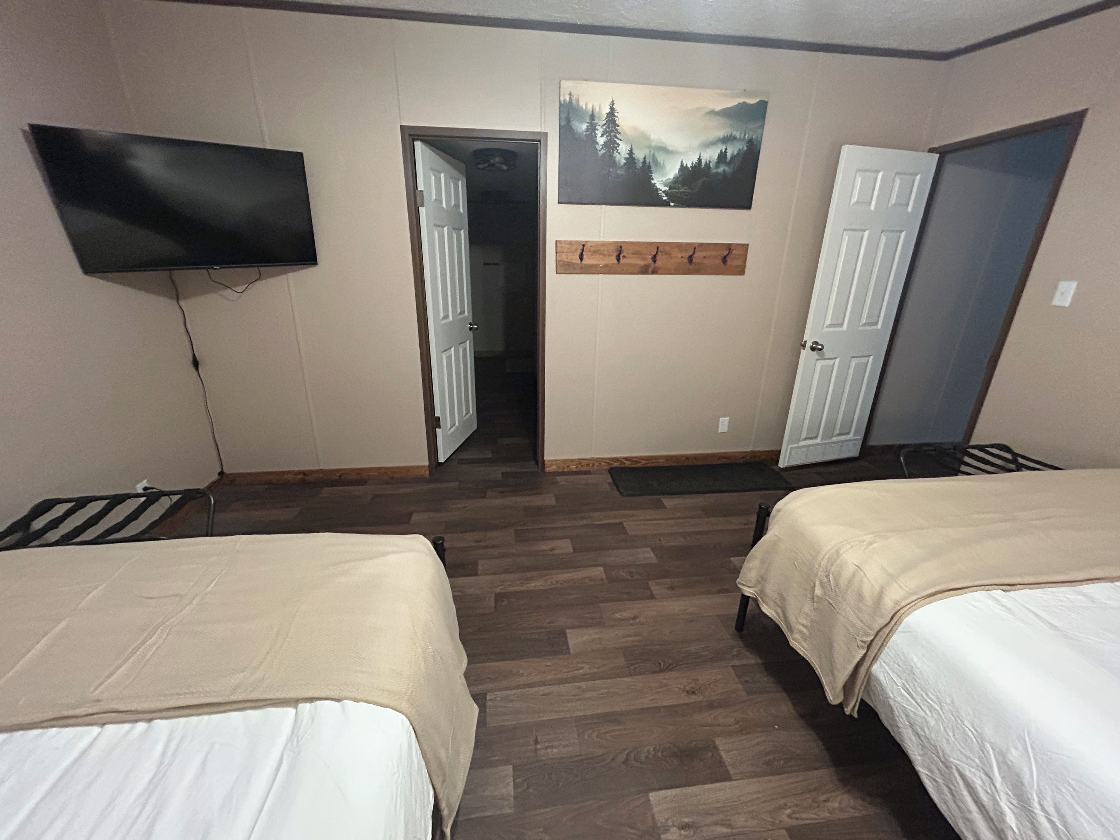 Ein Hotelzimmer mit zwei Betten, einem flachbildfernseher an der Wand und einem Gemälde über der Tür.