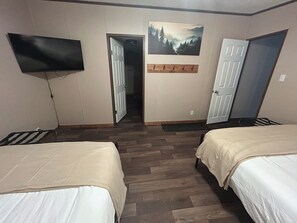 Habitación de hotel con dos camas, un televisor de pantalla plana en la pared y un cuadro sobre la puerta.