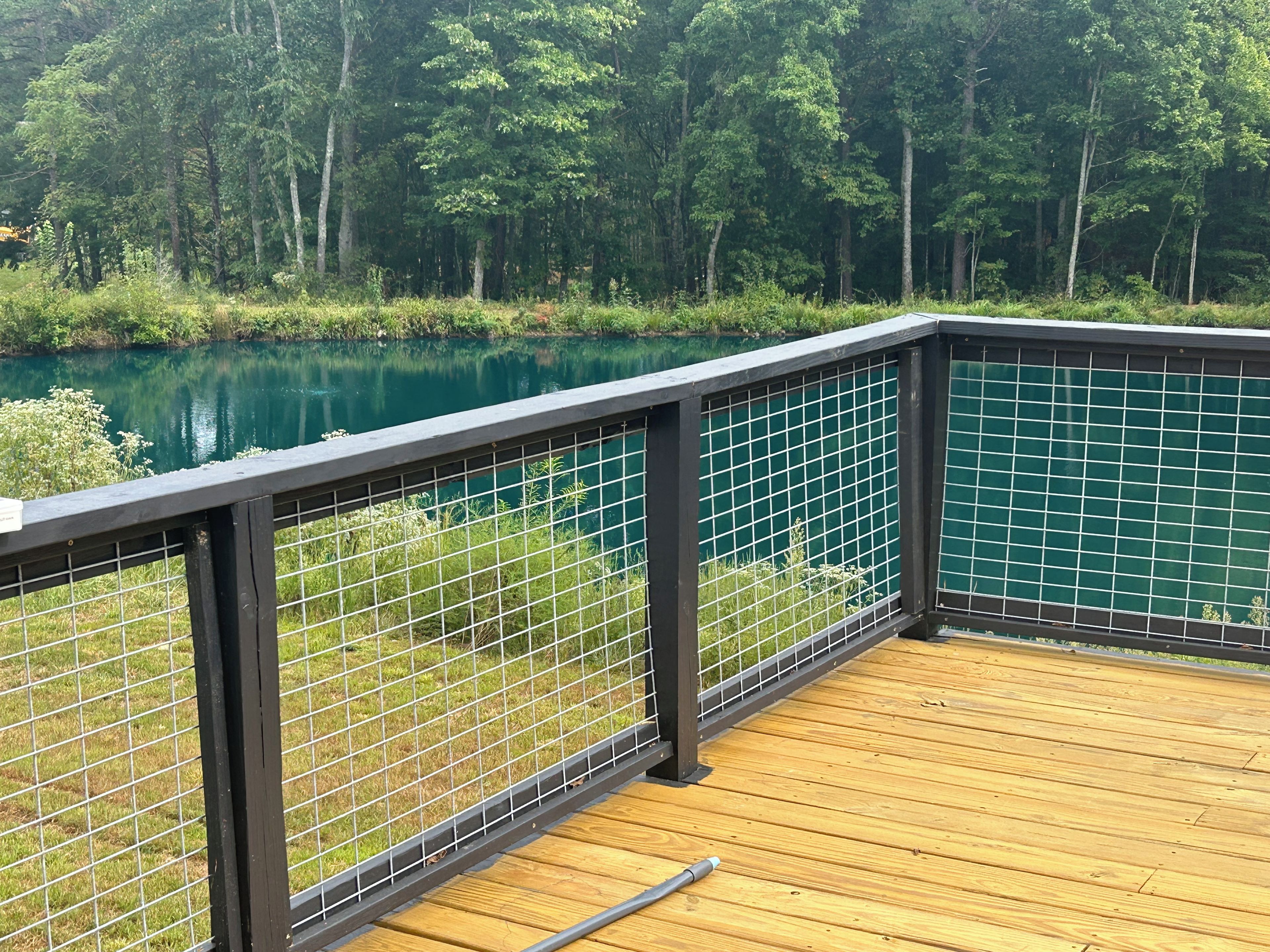 A wooden deck with a metal railing overlooking a lake surrounded by trees.
