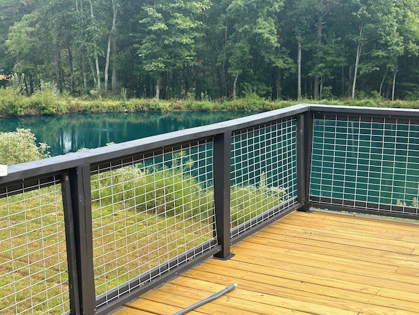 A wooden deck with a metal railing overlooking a lake surrounded by trees.