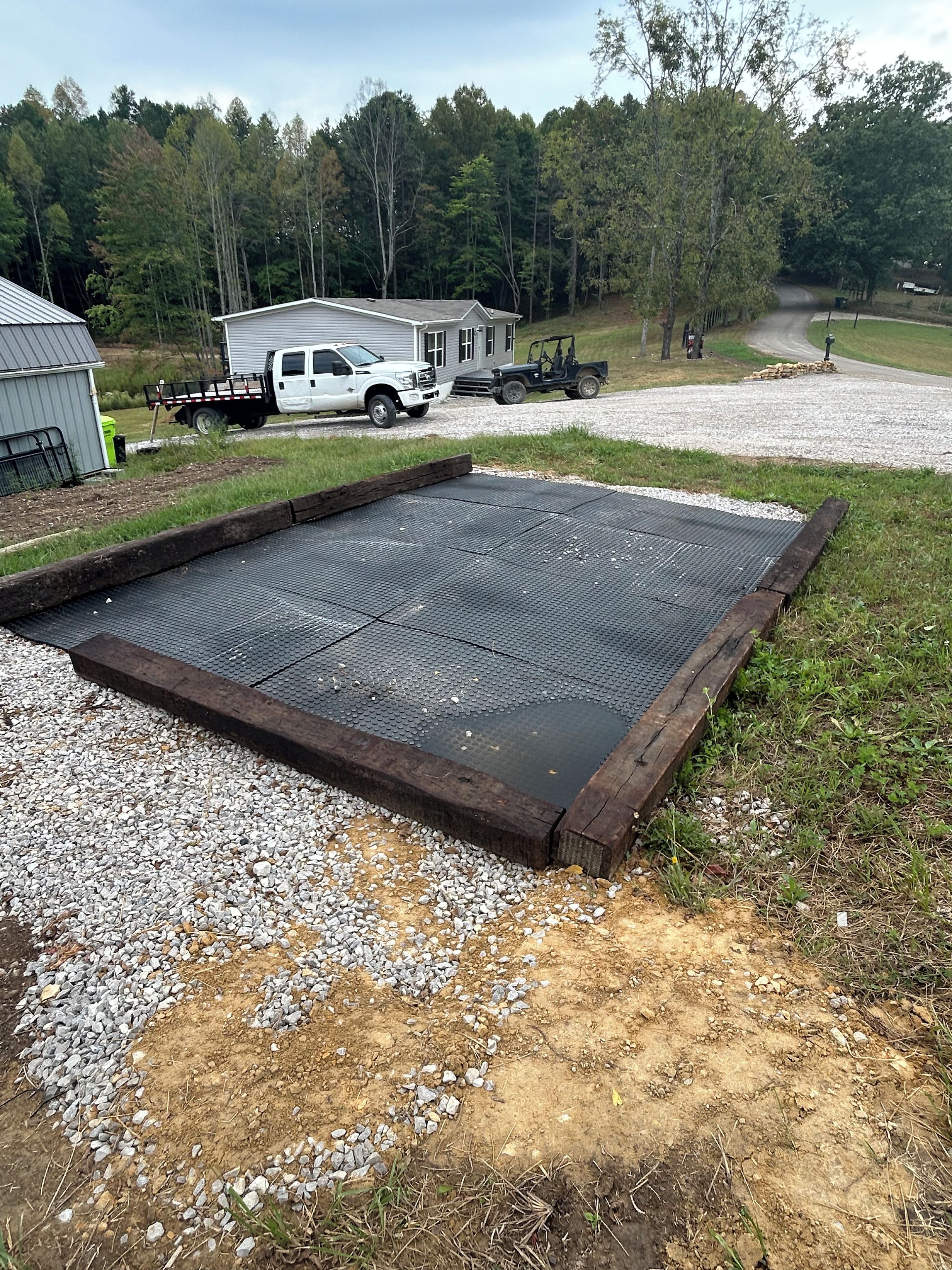 A gravel area with a metal grate, a white pickup truck, and a trailer in the background.