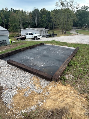 A gravel area with a metal grate, a white pickup truck, and a trailer in the background.