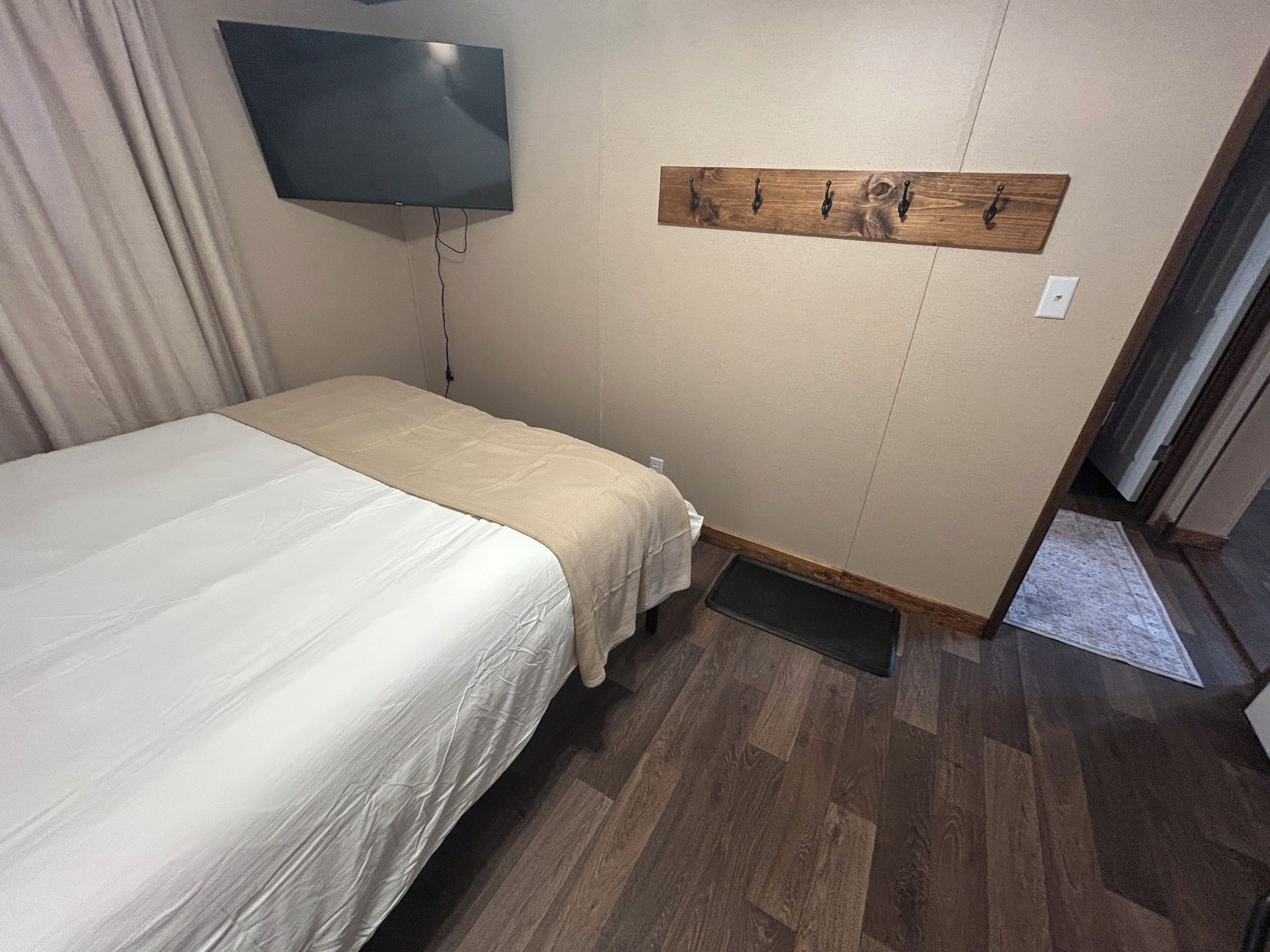 A hotel room with a bed, a flat-screen TV mounted on the wall, and a wooden coat rack.