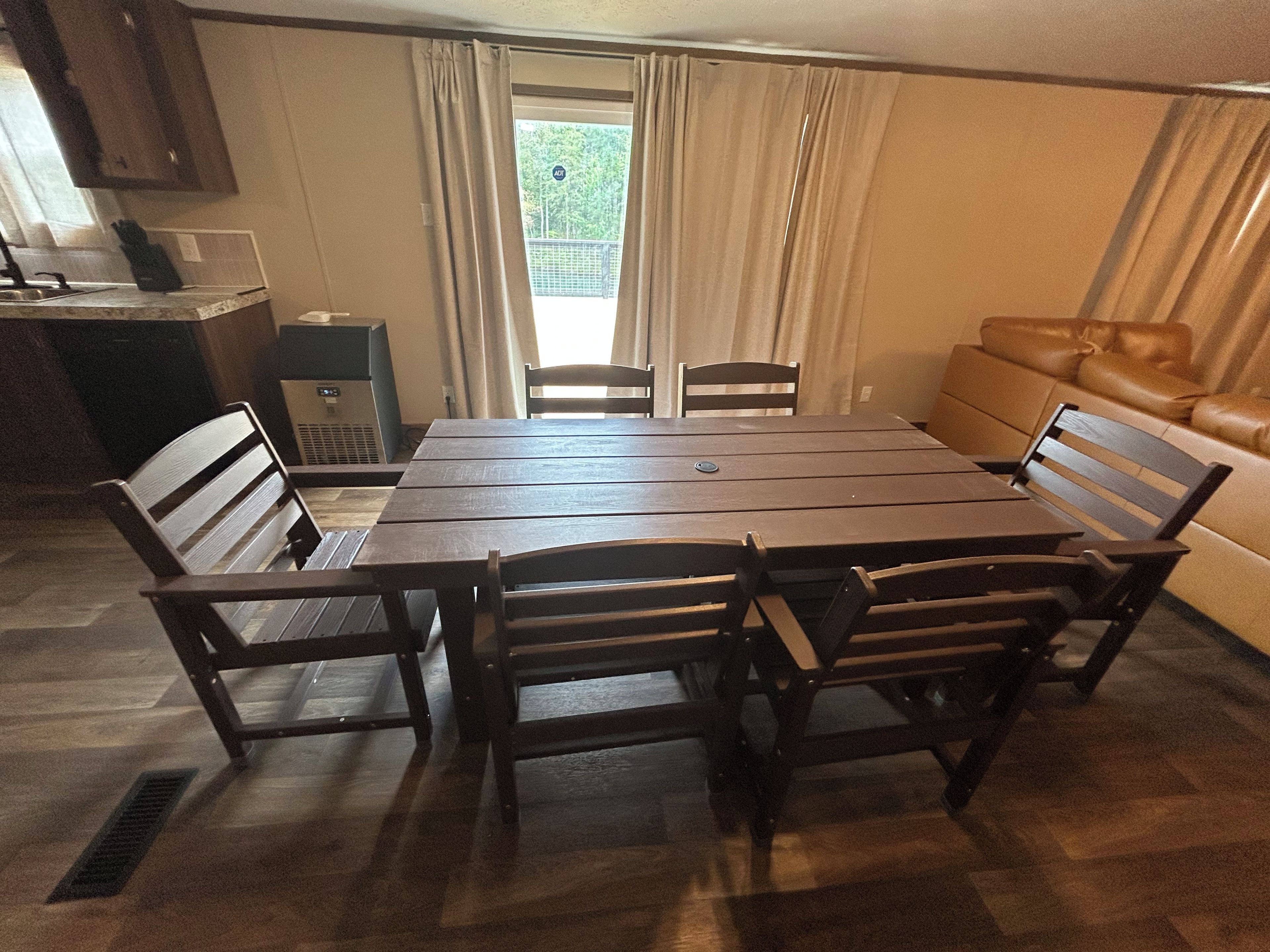 A dining area with a rectangular table surrounded by six chairs, a sofa, and a kitchen area with cabinets and appliances.