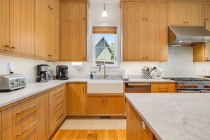 A kitchen with wooden cabinets, a stainless steel range, a sink, and a window with a view of a house. - Balsam Preserve Private Golf Resort | Luxury w/ Mtn Views (Sylva)