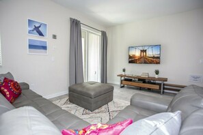 A modern living room with a grey sofa, a coffee table, and a TV on a wooden stand. - 5BR Storey Lake | Pool, Mickey & Minions rooms (Kissimmee)
