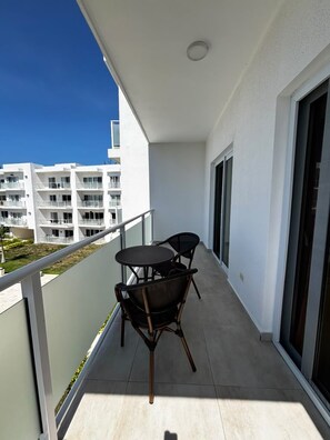 A balcony with a table and chairs, a view of a building complex, and a clear sky. - Sunset Vibes - Studio, pool views, resort access (Sosúa)