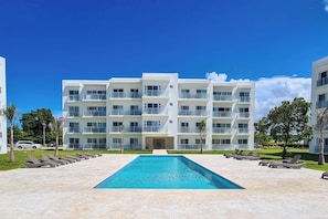 A modern multi-story hotel with a central swimming pool, surrounded by lounge chairs and greenery. - Sunset Vibes - Studio, pool views, resort access (Sosúa)