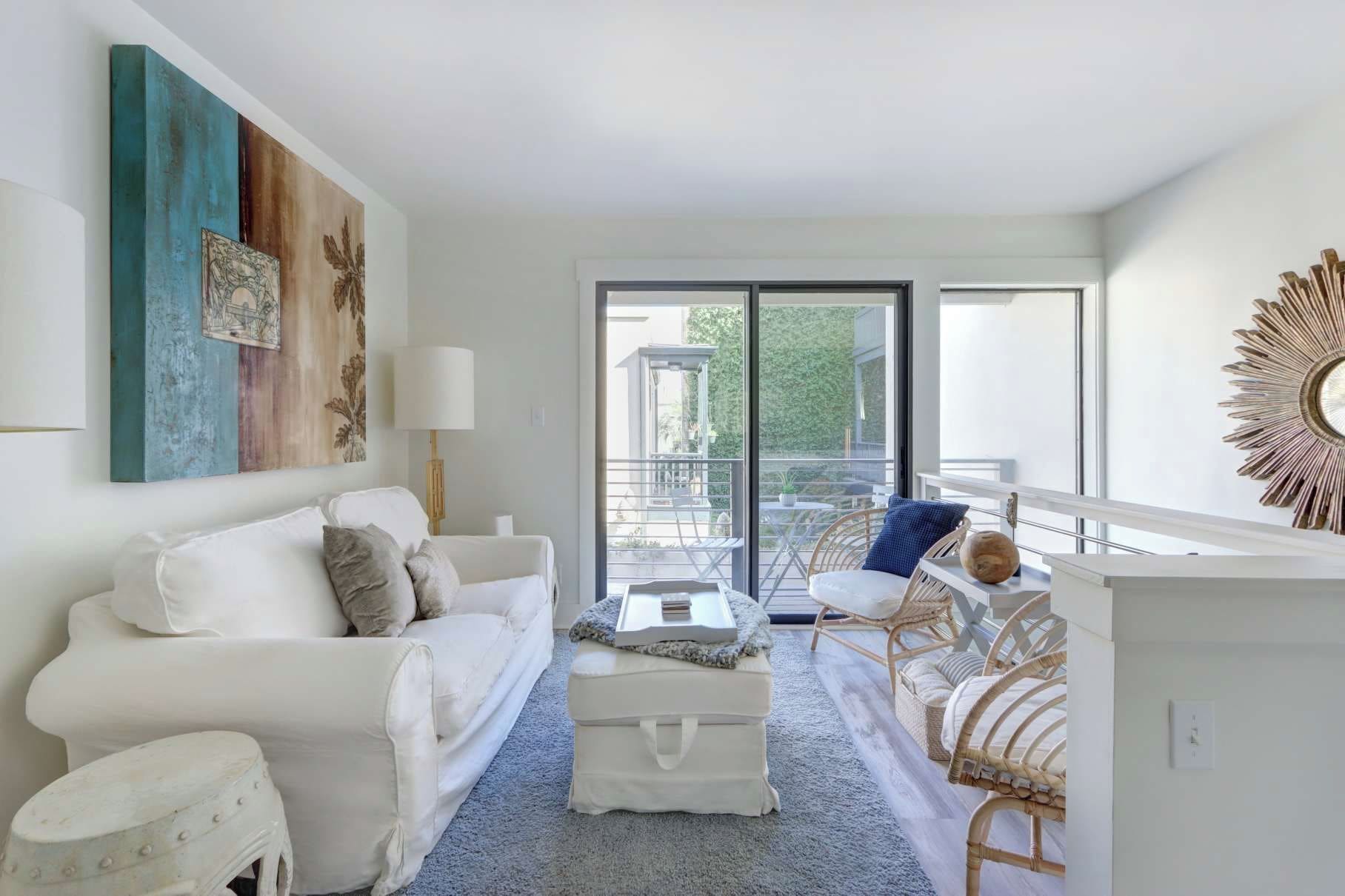 Un salon moderne avec un canapé blanc, une petite table et un balcon agrémenté de fauteuils en osier.
