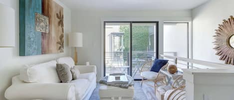 A modern living room with a white sofa, a small table, and a balcony with wicker chairs.