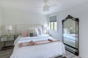 Ein Schlafzimmer mit Bett, Nachttischlampen, Deckenventilator, Fenster und einem großen Spiegel.